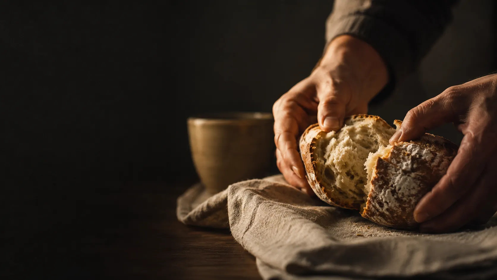 Hands breaking bread in warm light, symbolizing Catholic gratitude for ordinary blessings.
